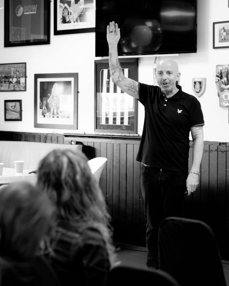 Lee Houghton, keynote speaker, on stage with his hand raised